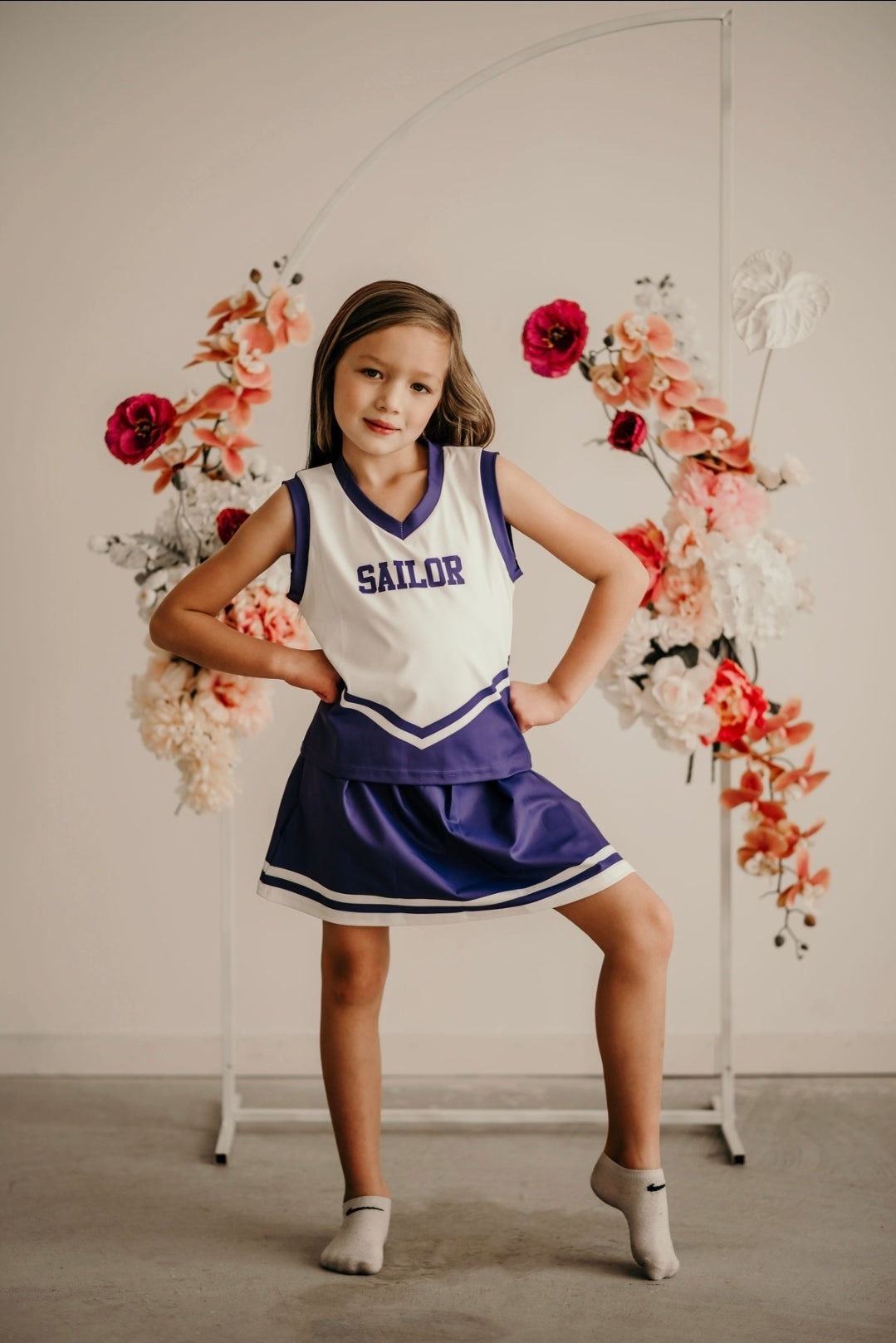 Young girl in a white and purple 3-piece cheer uniform, customizable with colors and name personalization.